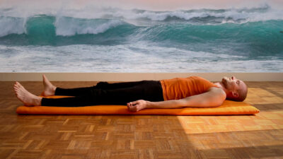 Homme en shavasana qui fait la respiration de vague avec les vagues de la mère au fond.