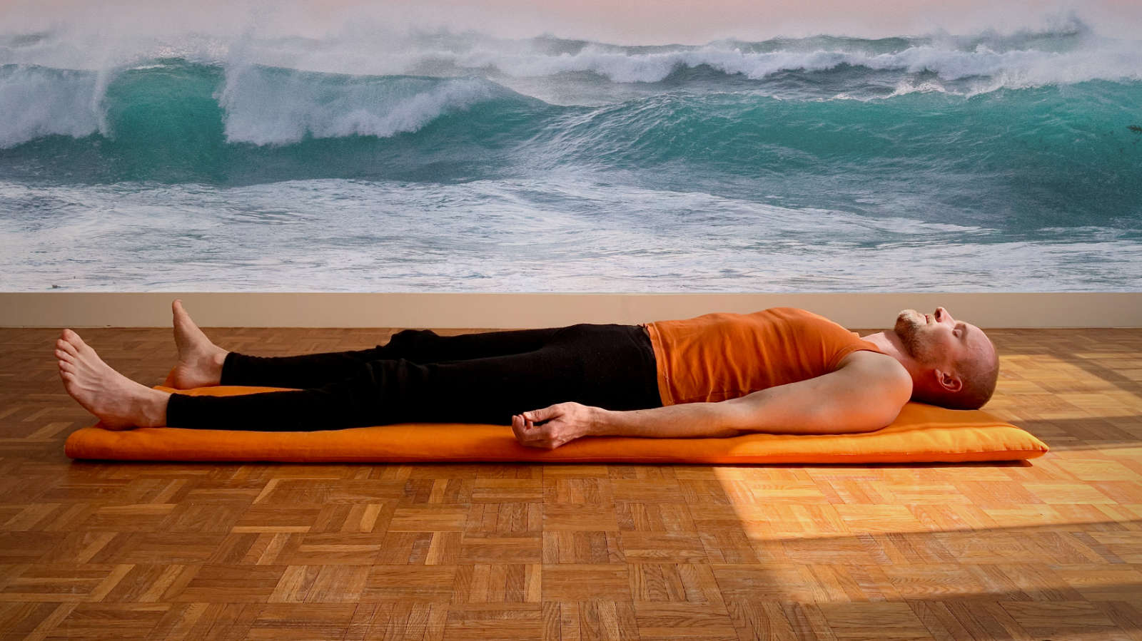 Homme en shavasana qui fait la respiration de vague avec les vagues de la mère au fond.