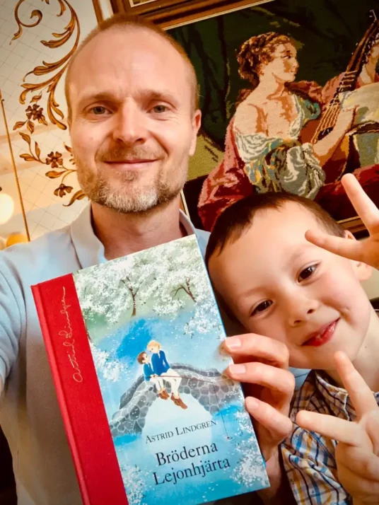 Un père lit Bröderna Lejonhjärta d’Astrid Lindgren avec son fils — un moment de lecture complice qui développe attention et imagination.