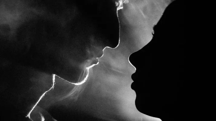 Deux profils presque en train de s’embrasser, leurs lèvres séparées par un souffle visible, symbolisant la tension et la retenue.