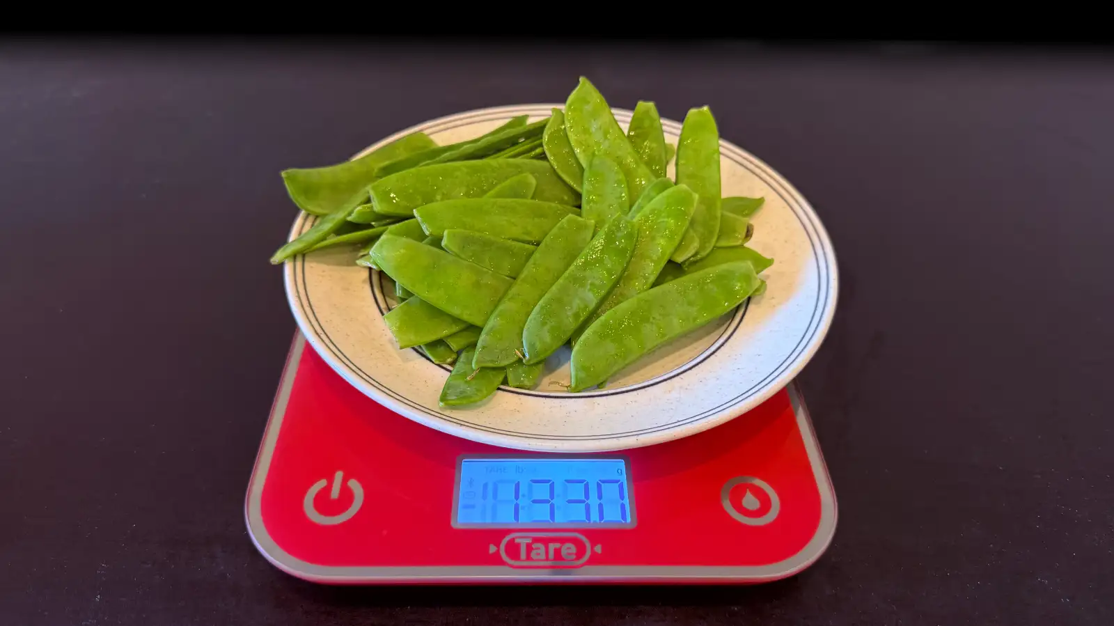 Assiette de pois gourmands posée sur une balance de cuisine affichant 133 grammes.