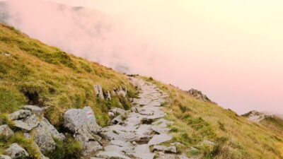 Sentier de montagne en pierre disparaissant dans la brume, éclairé par une douce lumière chaude.